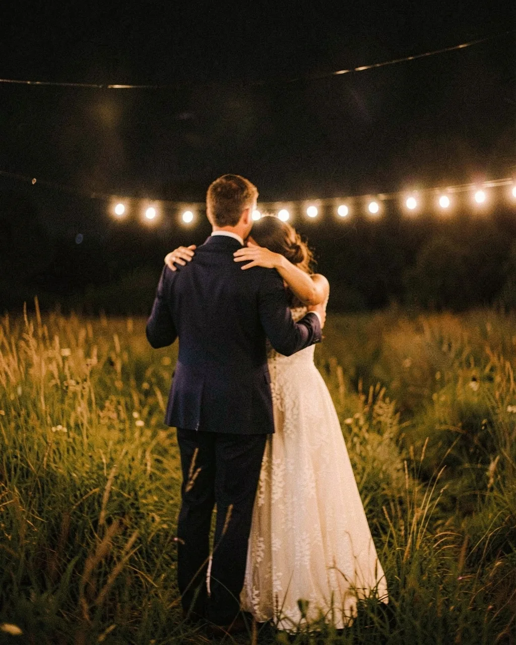 A couple dancing under string lights in a field at night