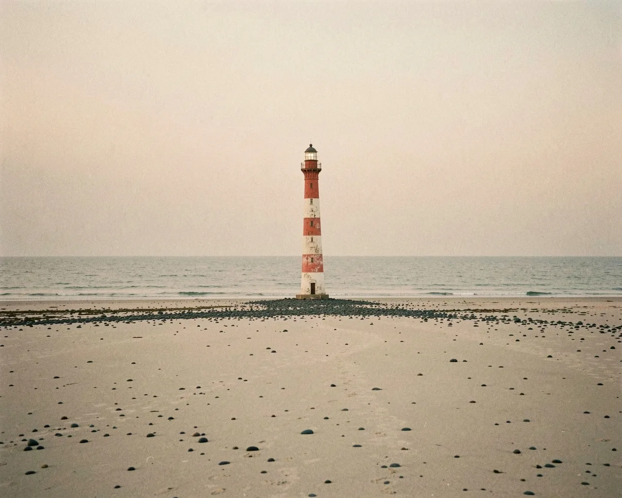 A red and white lighthouse on an empty beach