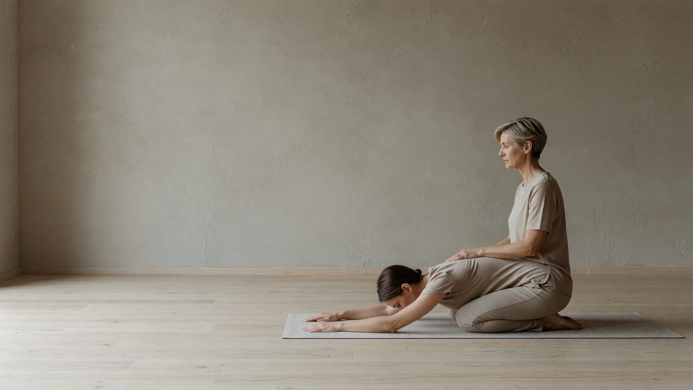 Anouk kneeling beside a student in child's pose, one hand on her lower back
