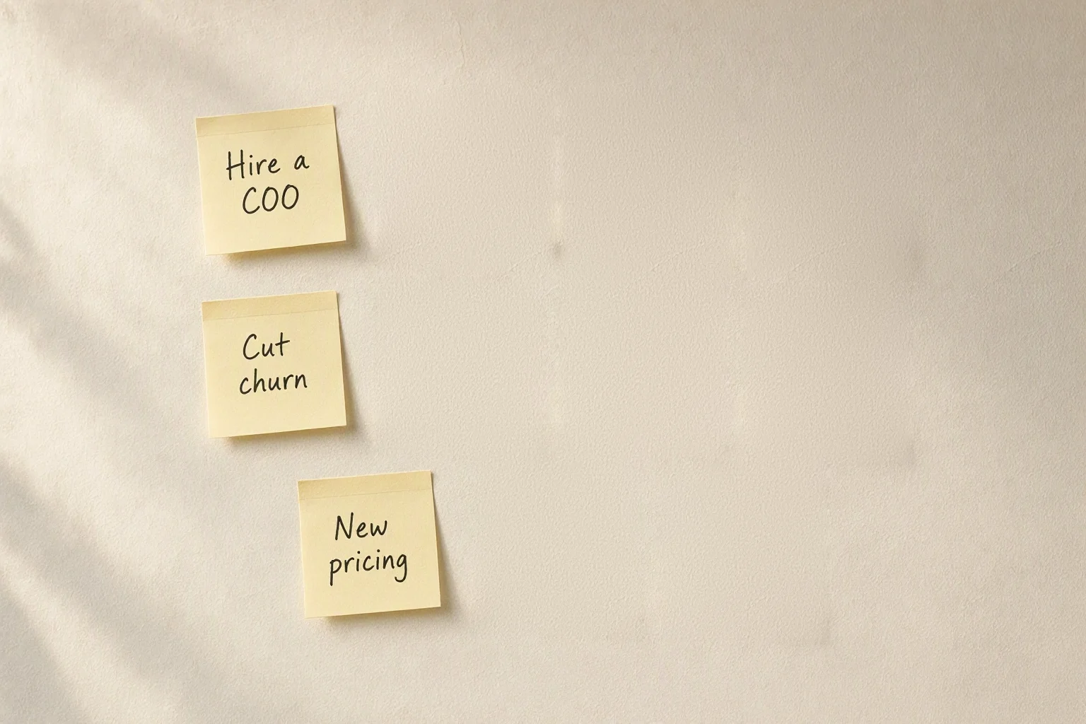 Three sticky notes left on a wall after a first session: Hire a COO, Cut churn, New pricing