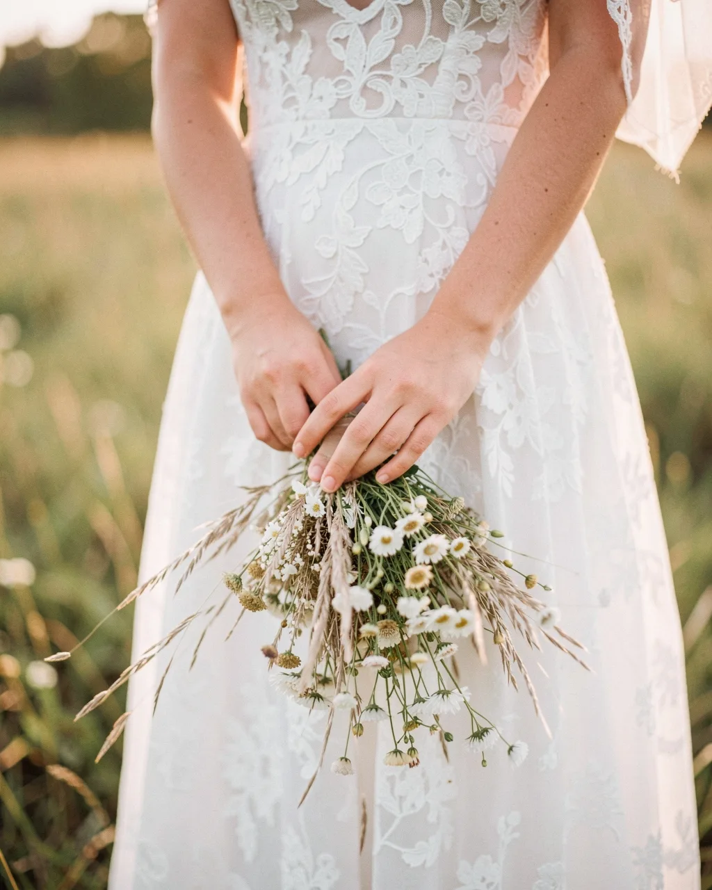 A bouquet of wild daisies and grasses held against a lace dress