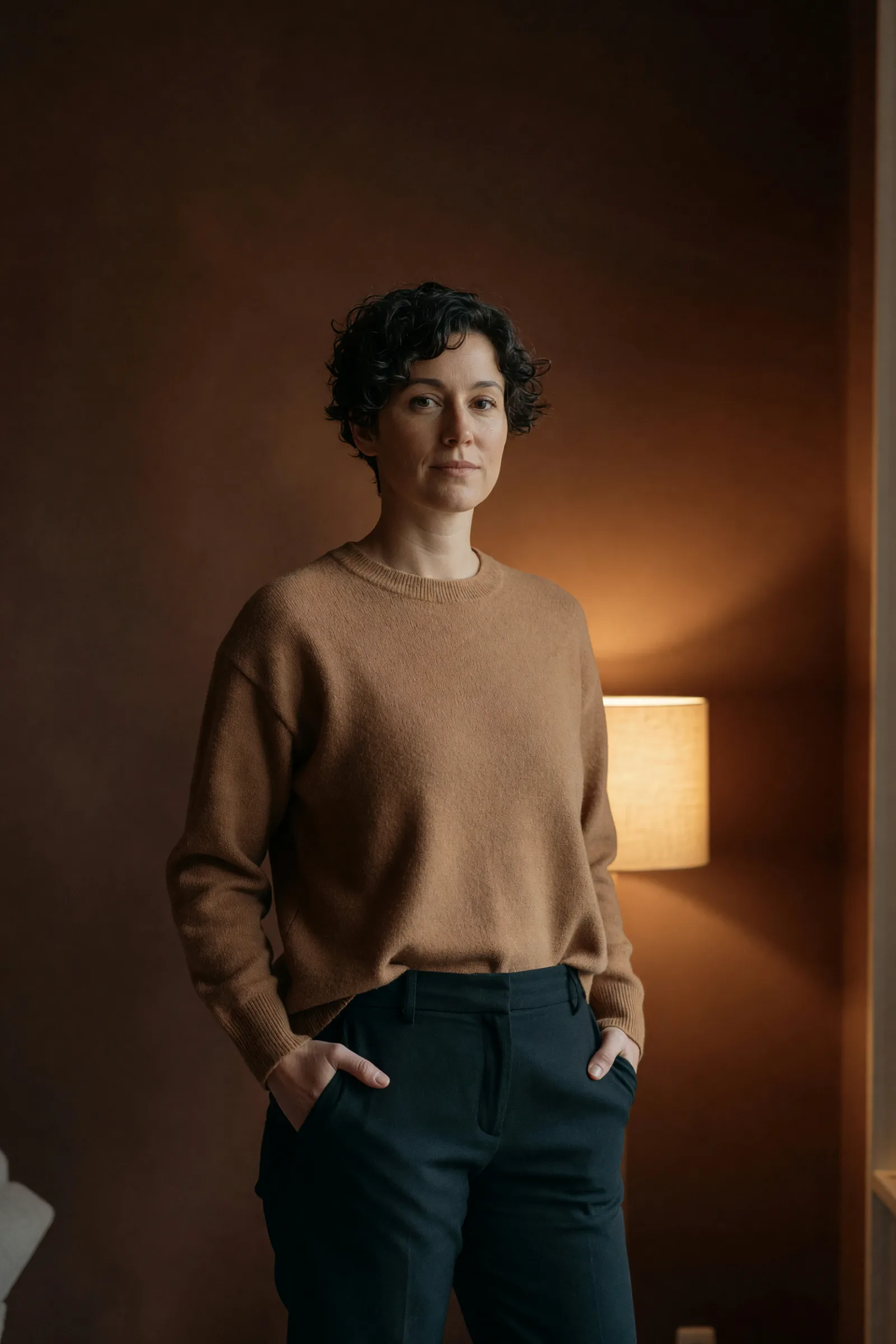 A customer standing in her living room beside a lit linen lamp