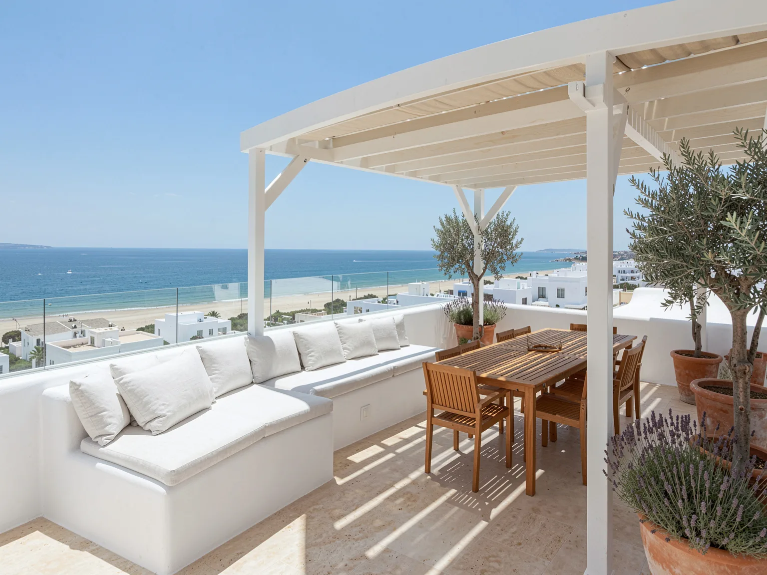A roof terrace with a pergola, olive trees and the beach below
