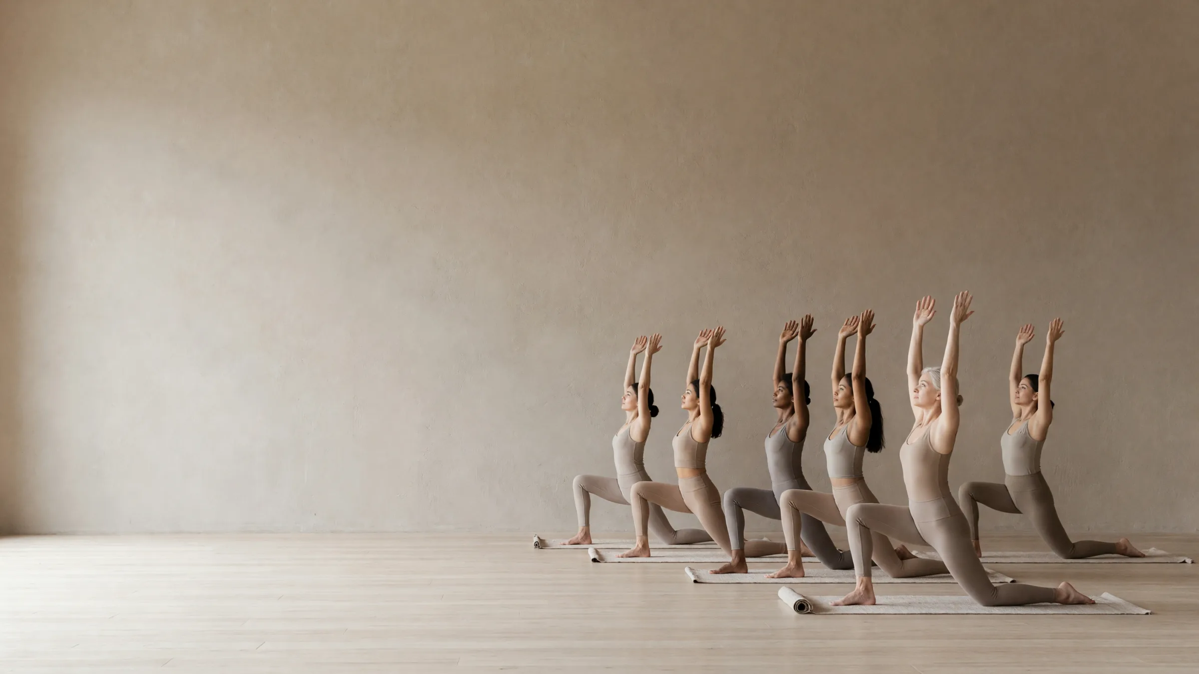 Six people in a low lunge with their arms raised, on linen mats across the studio