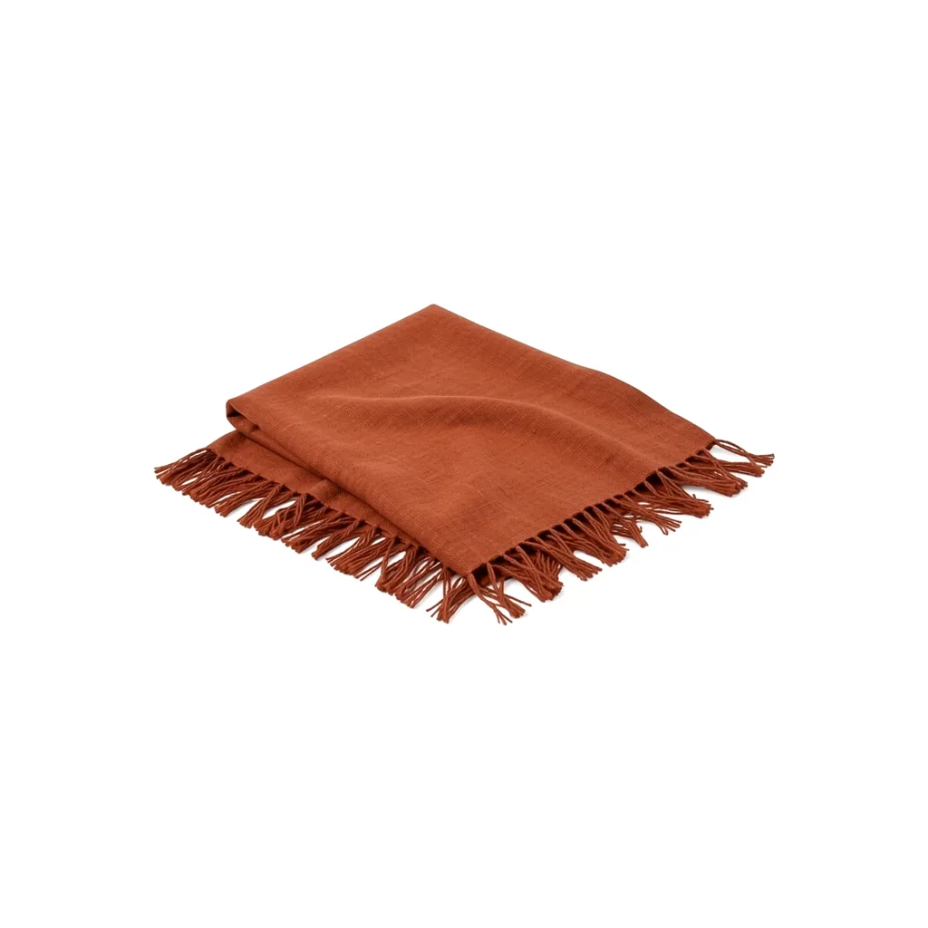 A folded rust linen throw with fringed edges