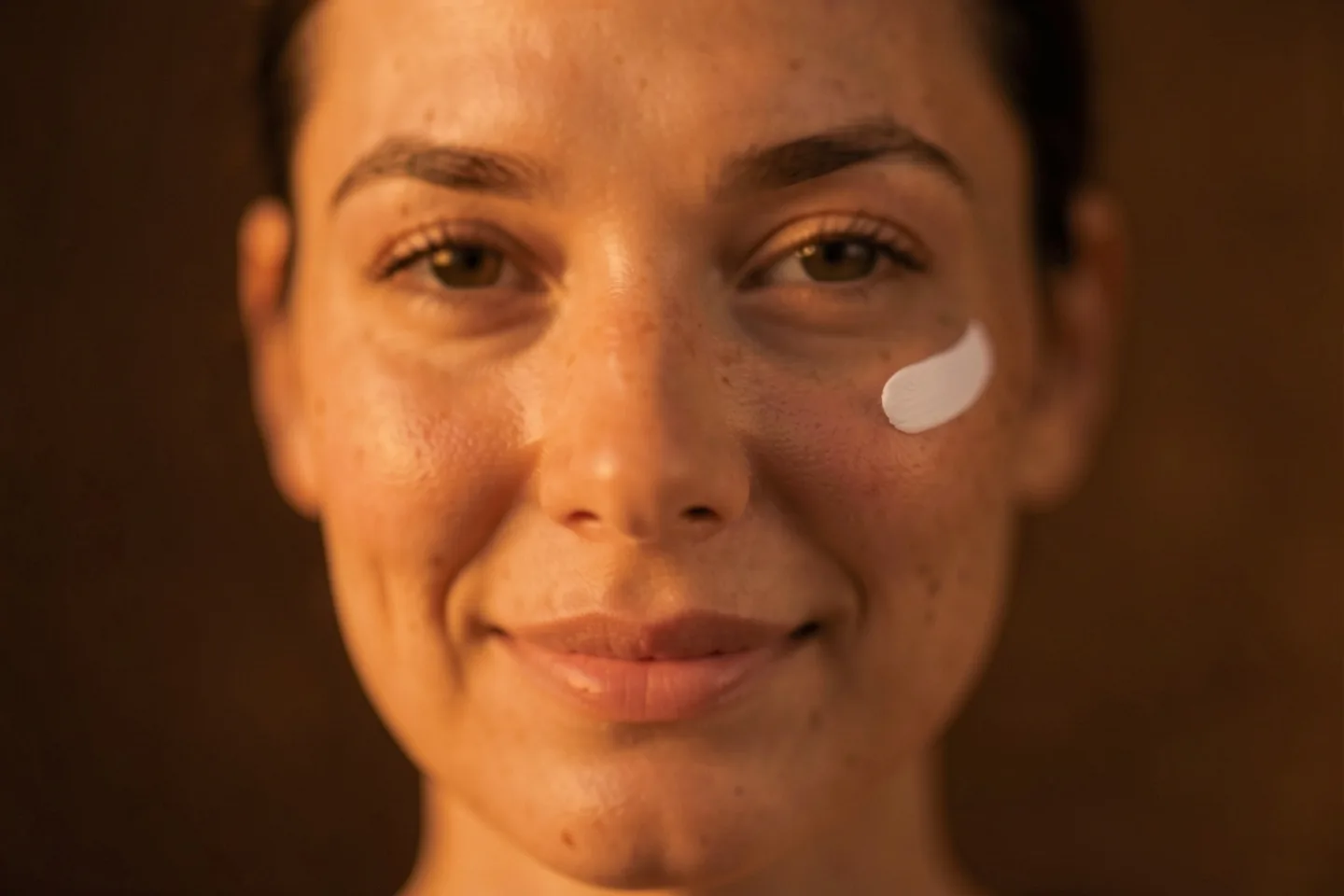A woman's face up close, with a dab of cream on her cheek